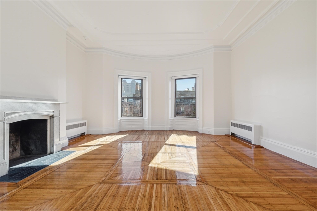 a view of an empty room with wooden floor fireplace and a window