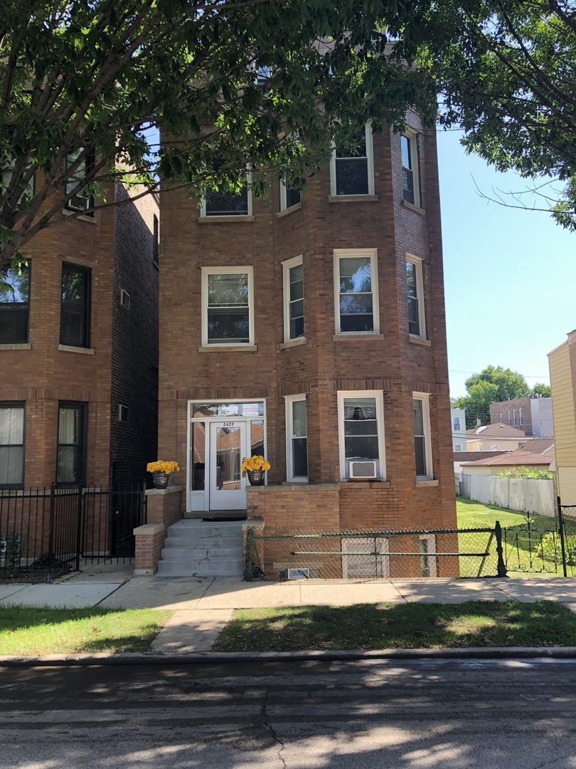 a view of a brick house with a yard plants and large tree