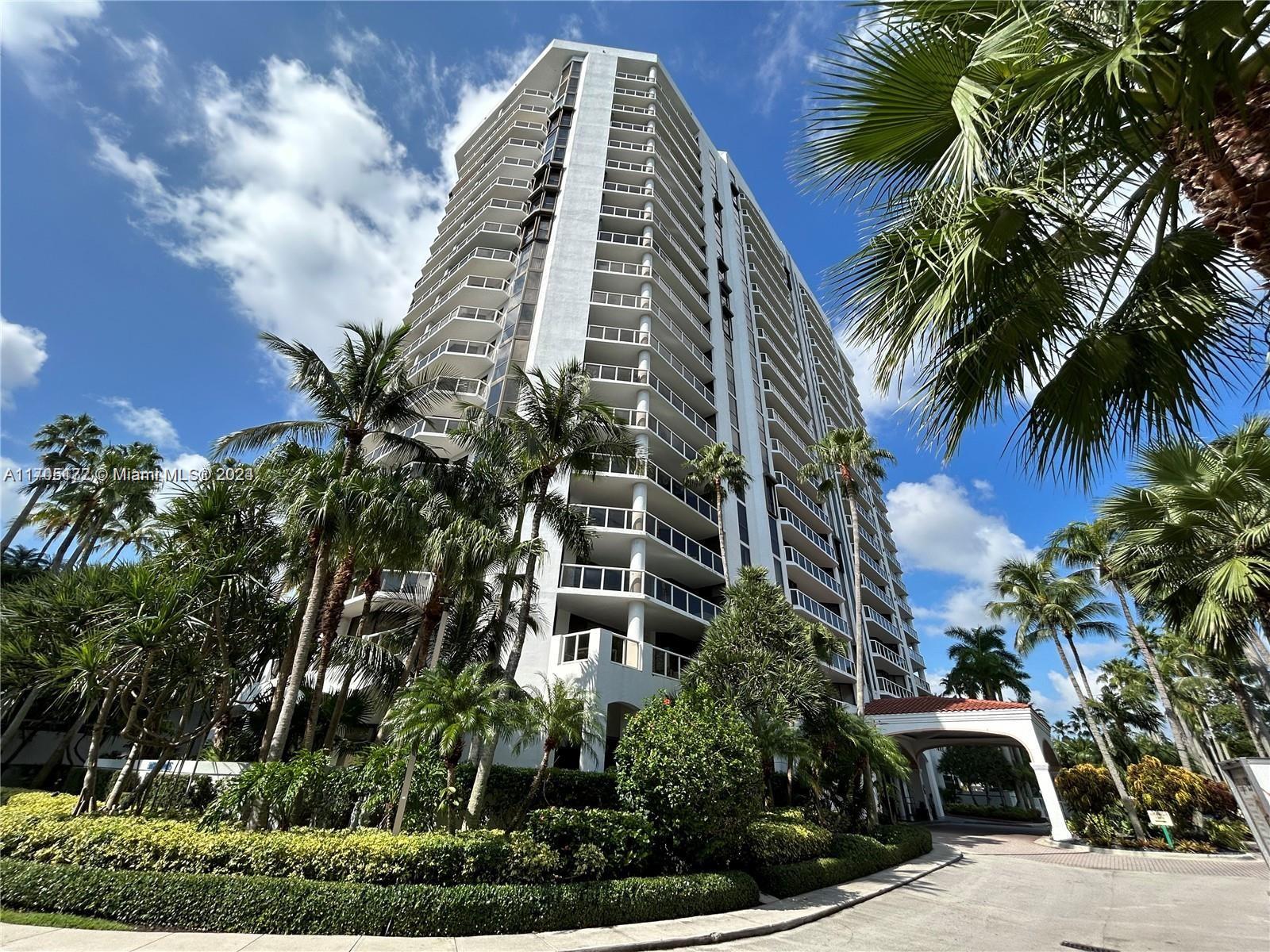 a view of a multi story residential apartment building with yard and parking space