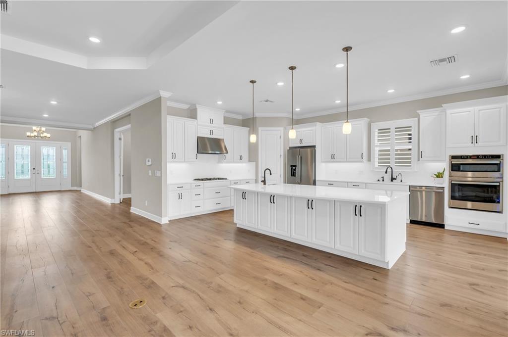 Kitchen featuring stainless steel appliances, pendant lighting, light wood-type flooring, and a center island