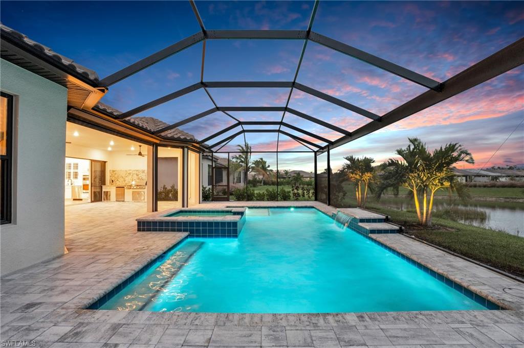 Pool at dusk featuring a water view, an in ground hot tub, a patio area, glass enclosure, and pool water feature