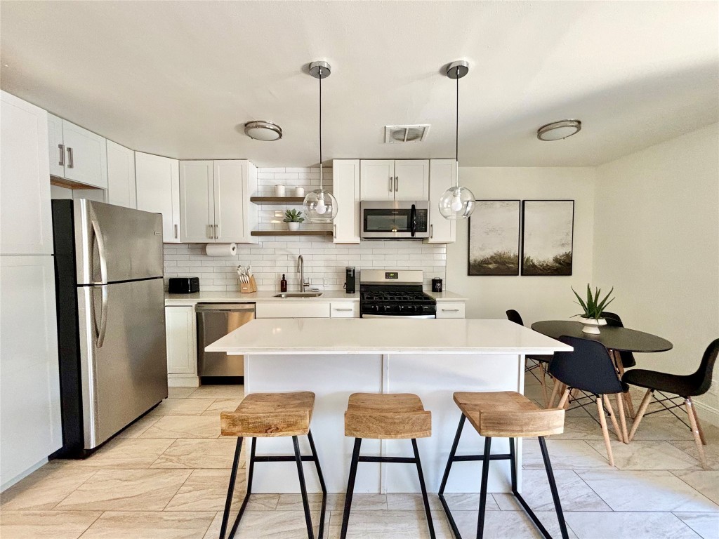 a kitchen with stainless steel appliances kitchen island granite countertop a refrigerator a stove a sink dishwasher a dining table and chairs with wooden floor