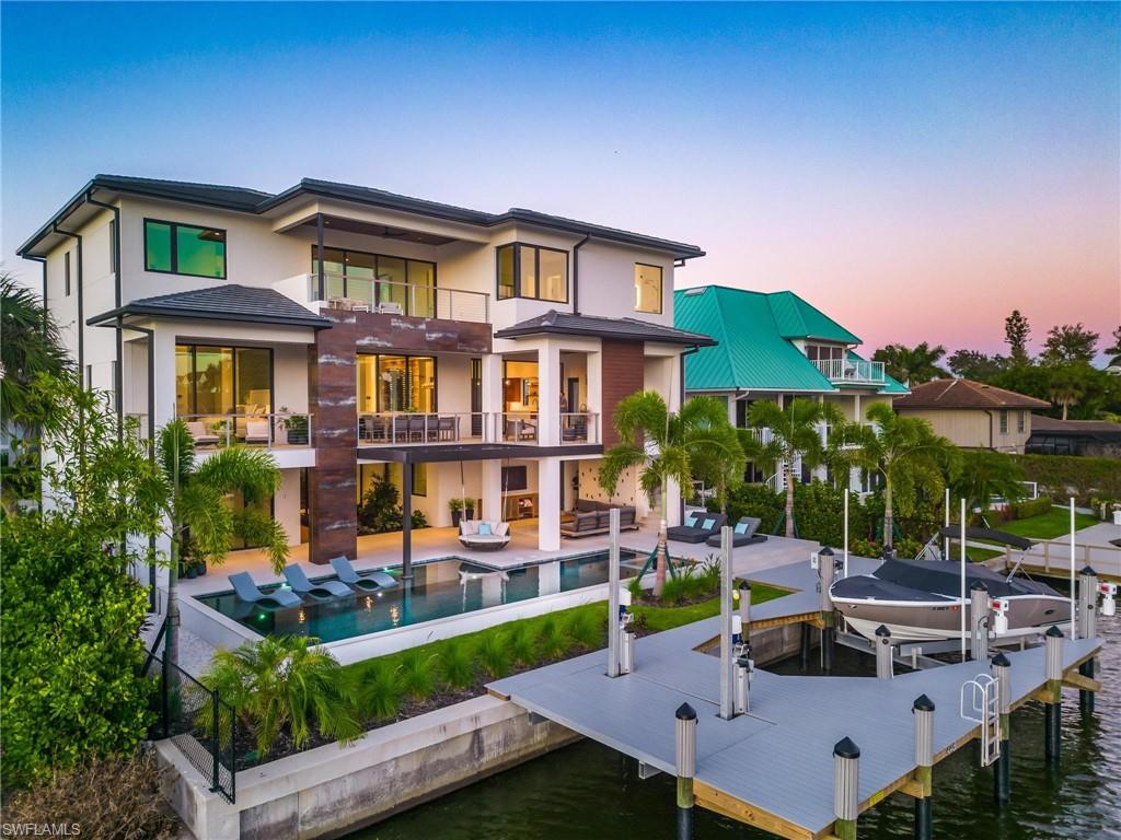 Back house at dusk with a pool with hot tub, a patio area, a balcony, and a water view