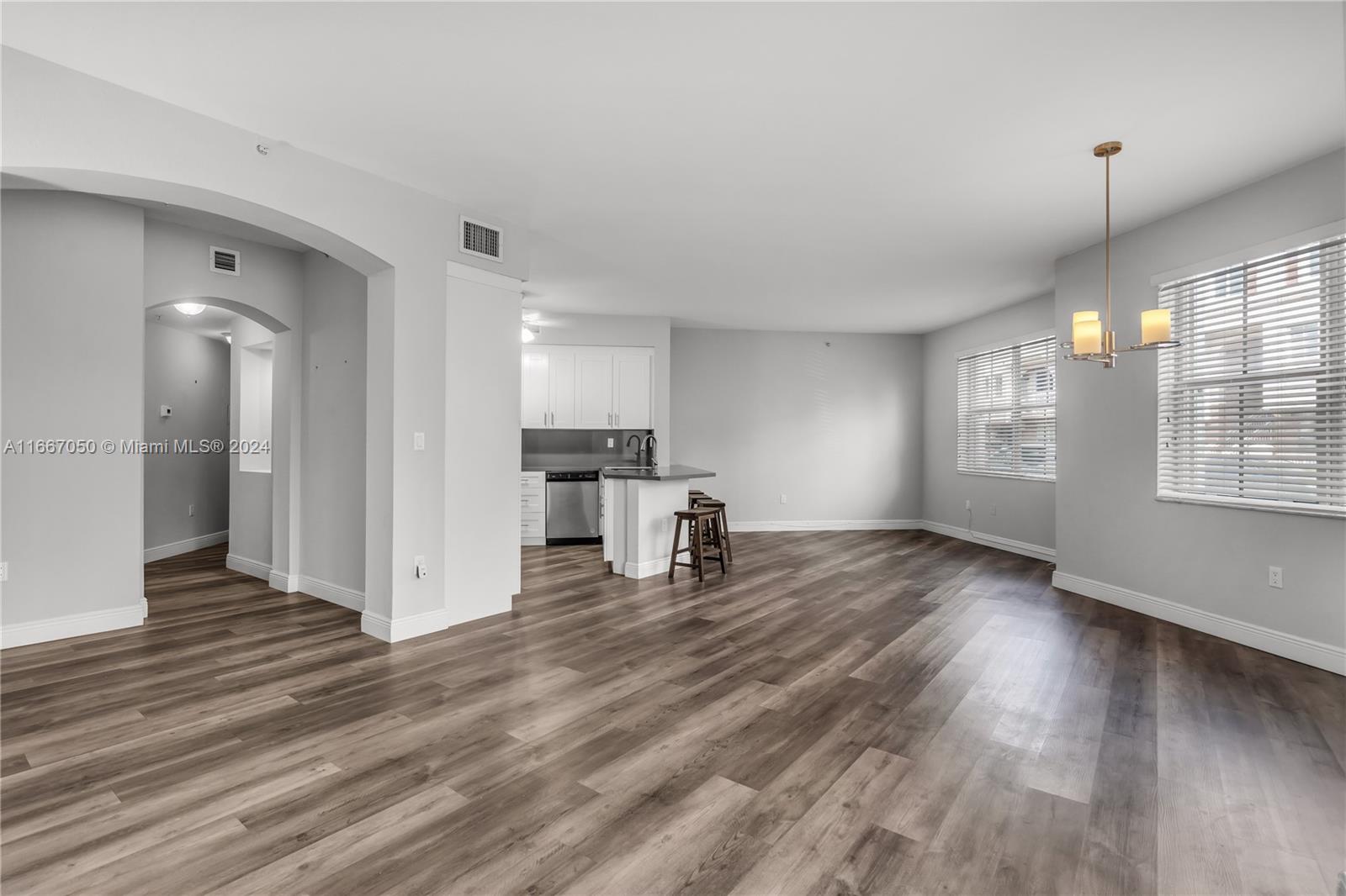 a view of empty room with wooden floor and kitchen view