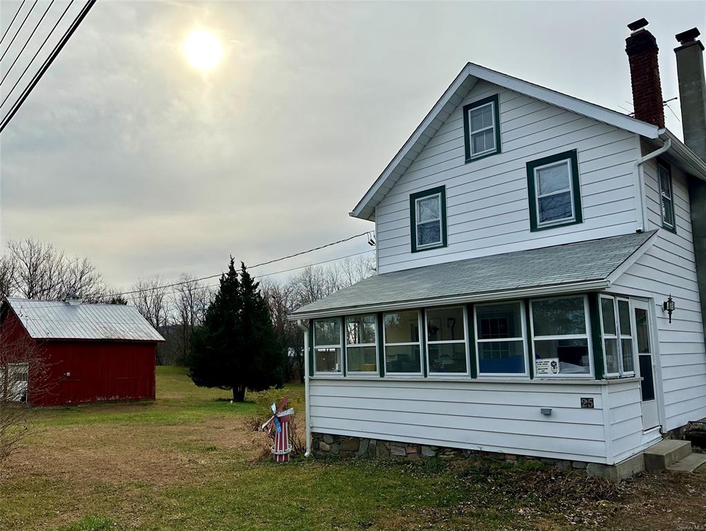 Back of house with a lawn, a sunroom, and a shed