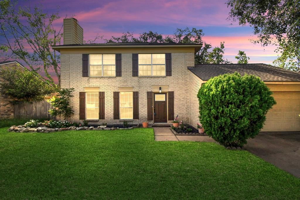 Charming two-story home with a well-manicured lawn and attached garage, featuring a classic brick facade and welcoming entryway, set against a beautiful twilight sky.