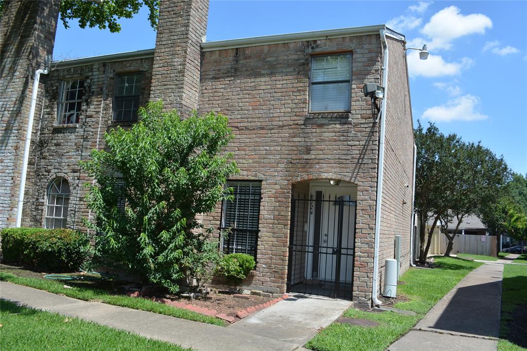 a brick house that has a small yard and large trees