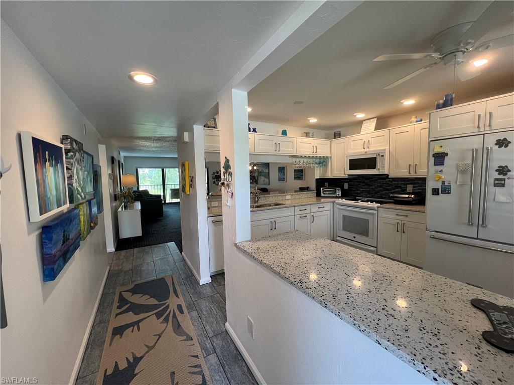 a large kitchen with stainless steel appliances granite countertop a large counter top a stove a sink dishwasher a refrigerator and white cabinets with wooden floor