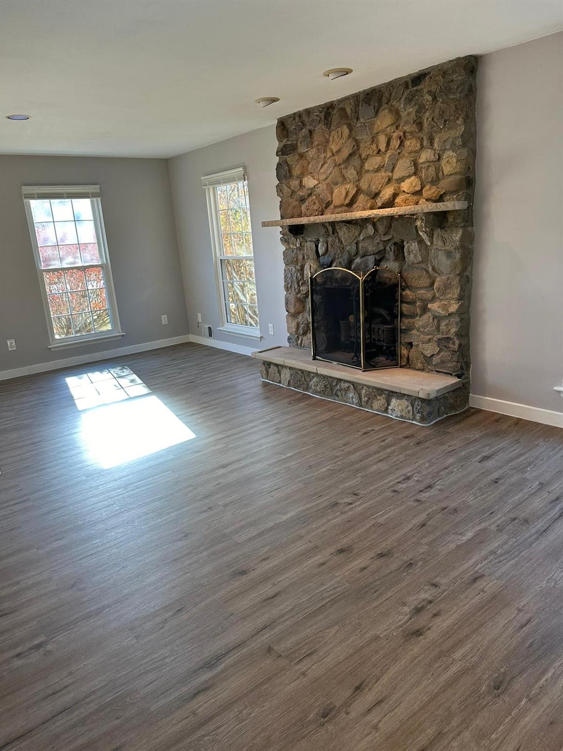 Living room featuring plenty of natural light, brand new vinyl plank flooring and a stone fireplace