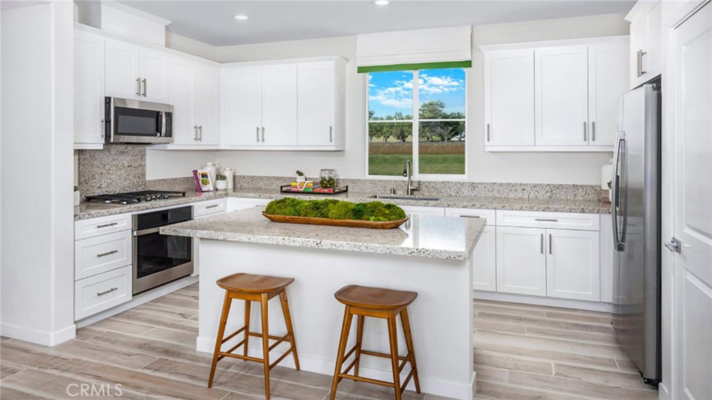 a kitchen with stainless steel appliances granite countertop white cabinets a sink a stove a dining table and chairs