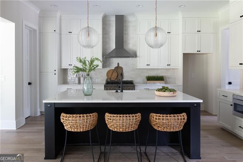 Kitchen with a large island with sink, decorative backsplash, white cabinetry, and wall chimney exhaust hood