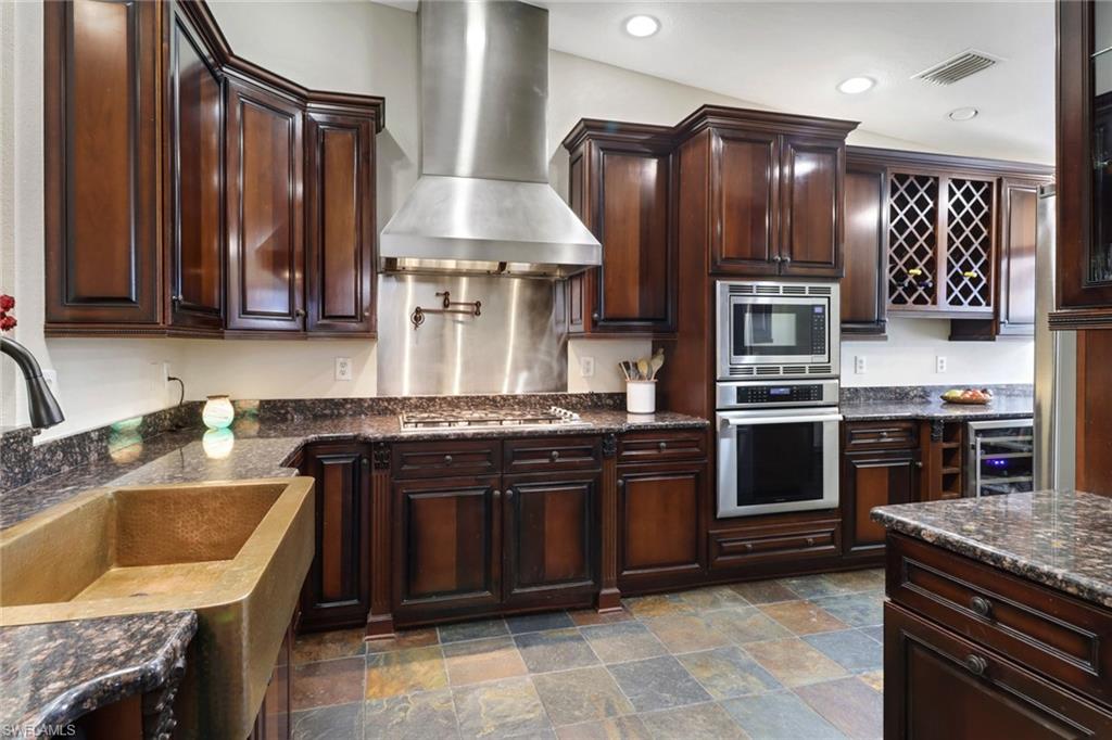 Kitchen featuring wall chimney range hood, sink, stainless steel appliances, dark brown cabinetry, and beverage cooler