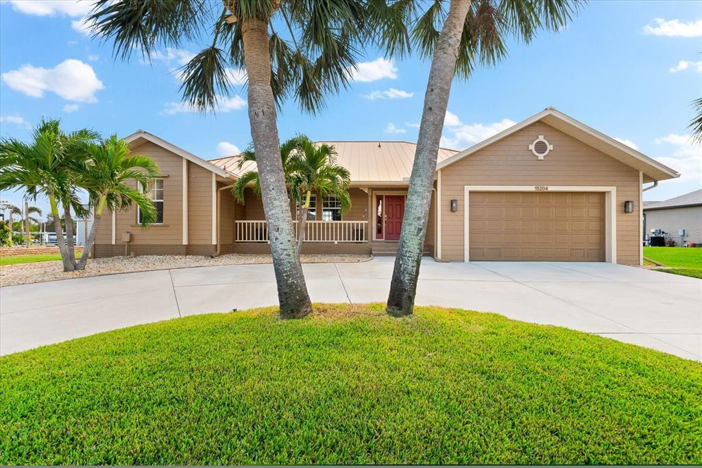 a front view of yellow house with a yard and palm trees