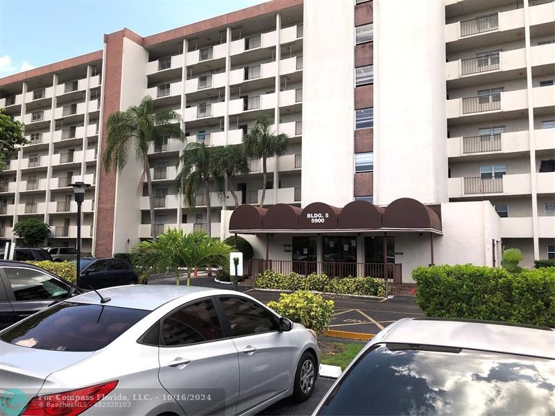 a front view of a building with parking space and couple of cars parked in front of it