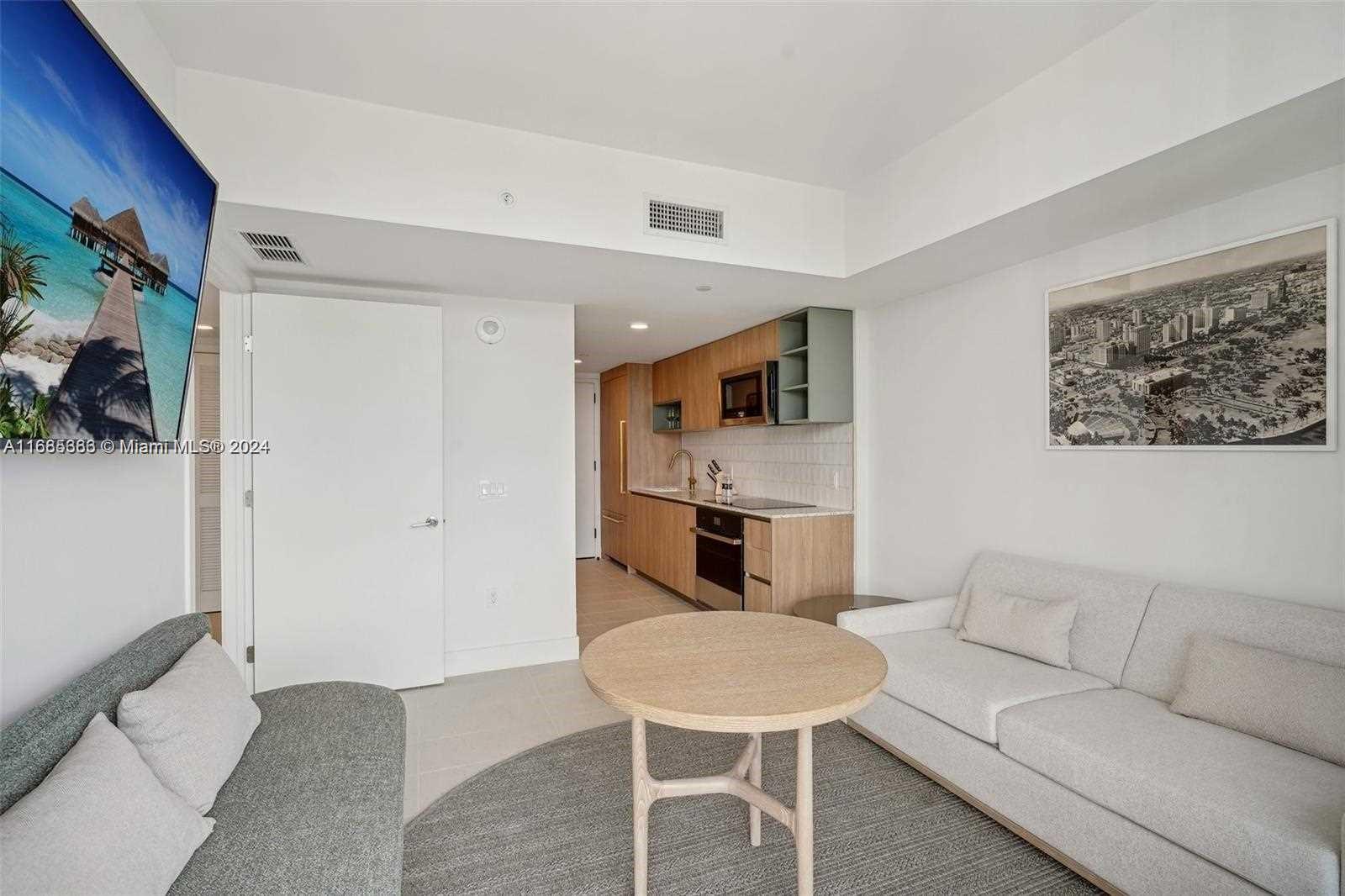 a living room with stainless steel appliances furniture a rug and a kitchen view