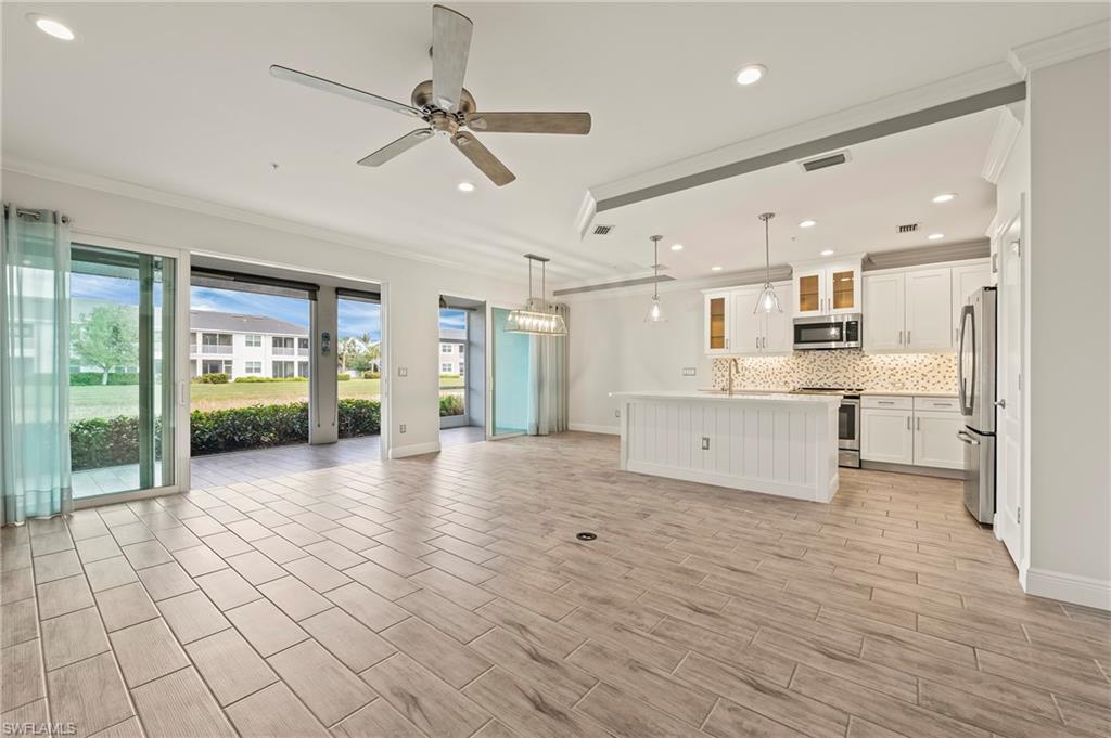 Kitchen with light wood-type flooring, stainless steel appliances, pendant lighting, white cabinets, and a kitchen island