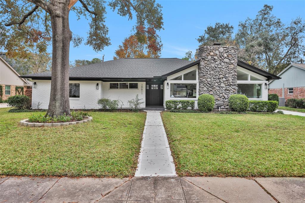 Charming single-story home with a modern exterior, featuring a striking stone chimney. The house is surrounded by a well-maintained lawn and mature trees, offering great curb appeal. Large windows provide ample natural light, enhancing the inviting atmosphere.