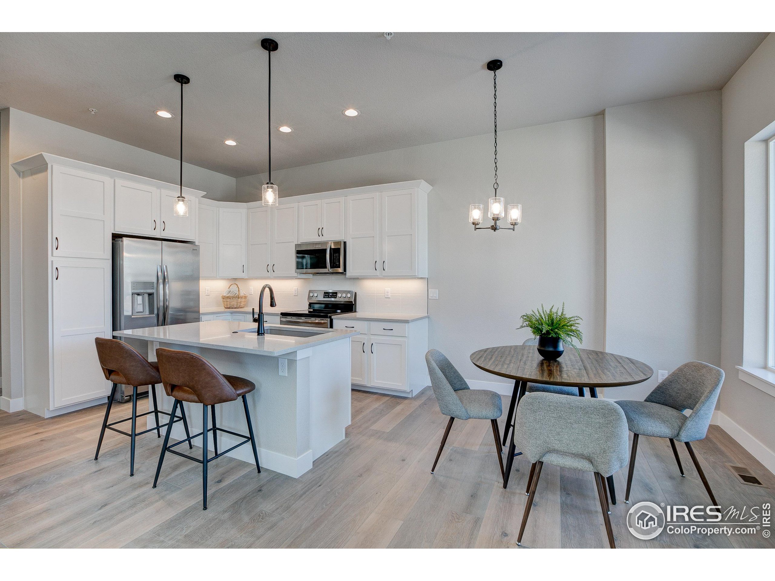 a open kitchen with stainless steel appliances kitchen island granite countertop a dining table chairs and white cabinets