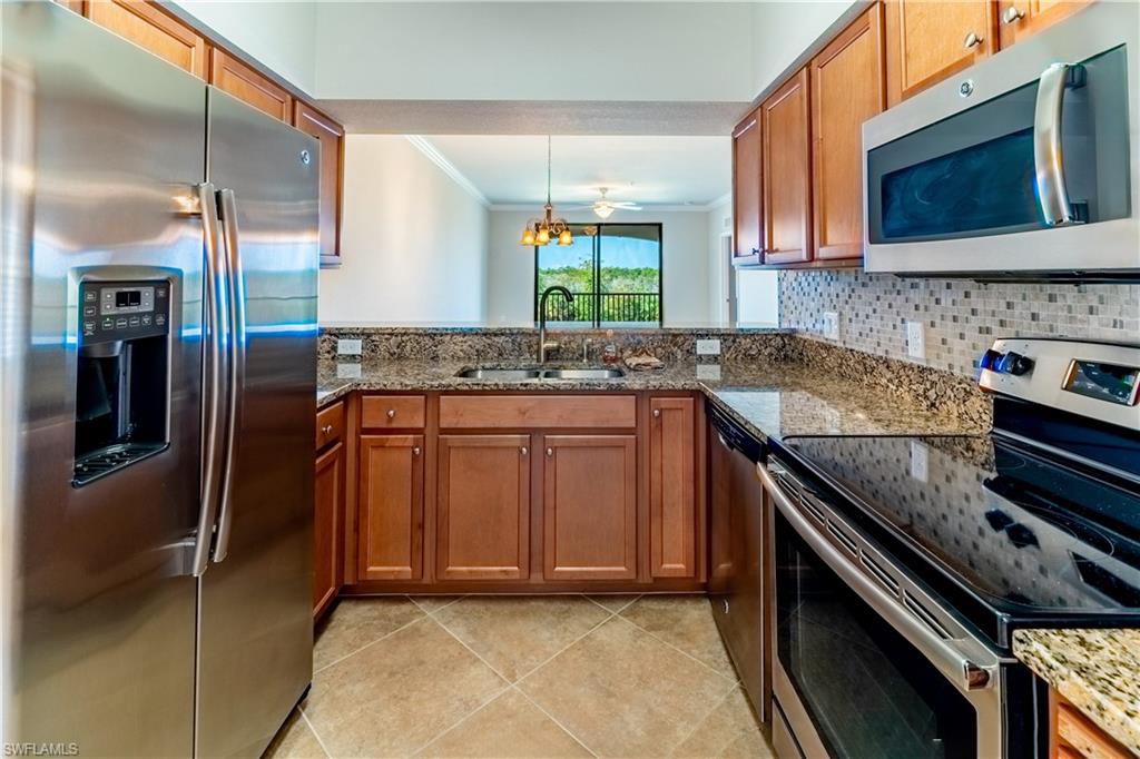 Kitchen featuring appliances with stainless steel finishes, light tile patterned floors, stone countertops, sink, and kitchen peninsula