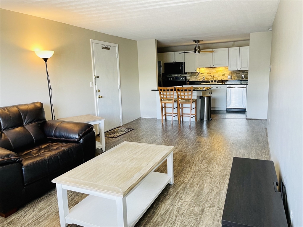 a living room with stainless steel appliances furniture a rug and a kitchen view