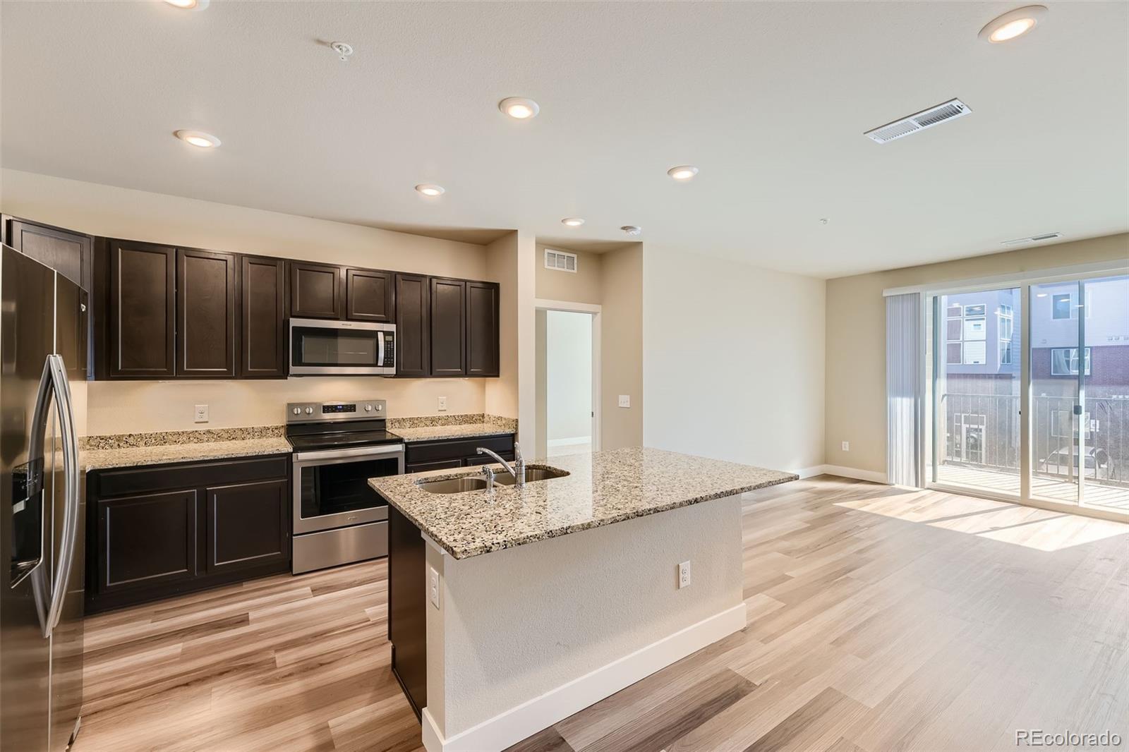 a kitchen with stainless steel appliances granite countertop a stove top oven a sink dishwasher a refrigerator and white cabinets with wooden floor