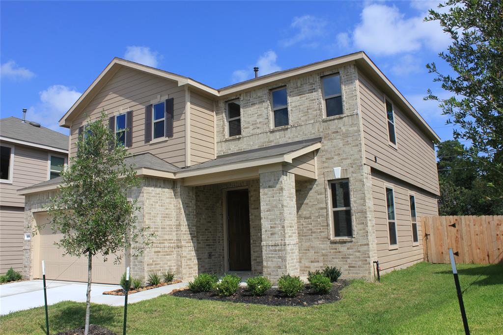 This is a modern two-story house with a mix of brick and siding exterior, featuring a covered entryway and a well-kept front lawn. The home sits on a corner lot with a wooden privacy fence and a small tree in the front yard.