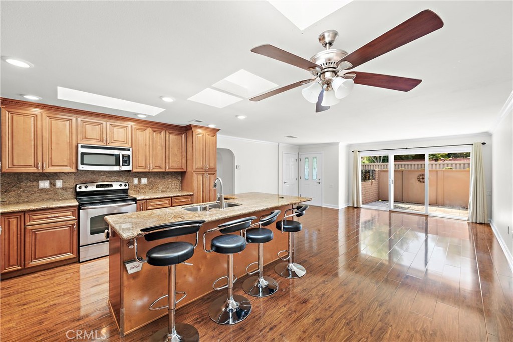 a kitchen with stainless steel appliances kitchen island granite countertop a stove a refrigerator a sink a dining table and chairs with wooden floor