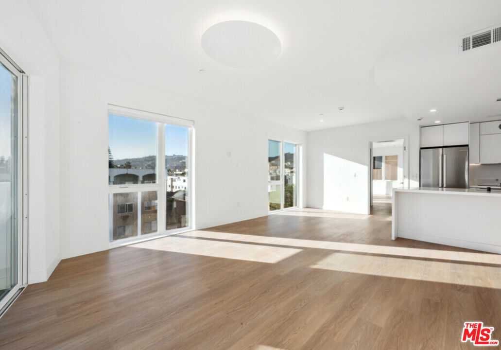 a view of an empty room with wooden floor and kitchen view