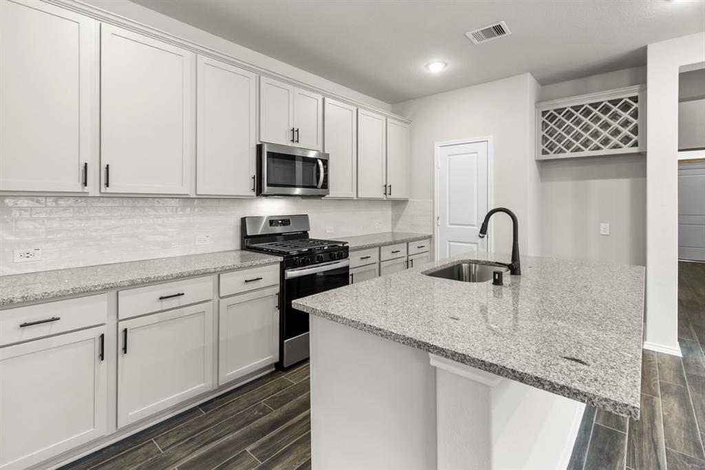 a kitchen with granite countertop a sink stainless steel appliances and white cabinets