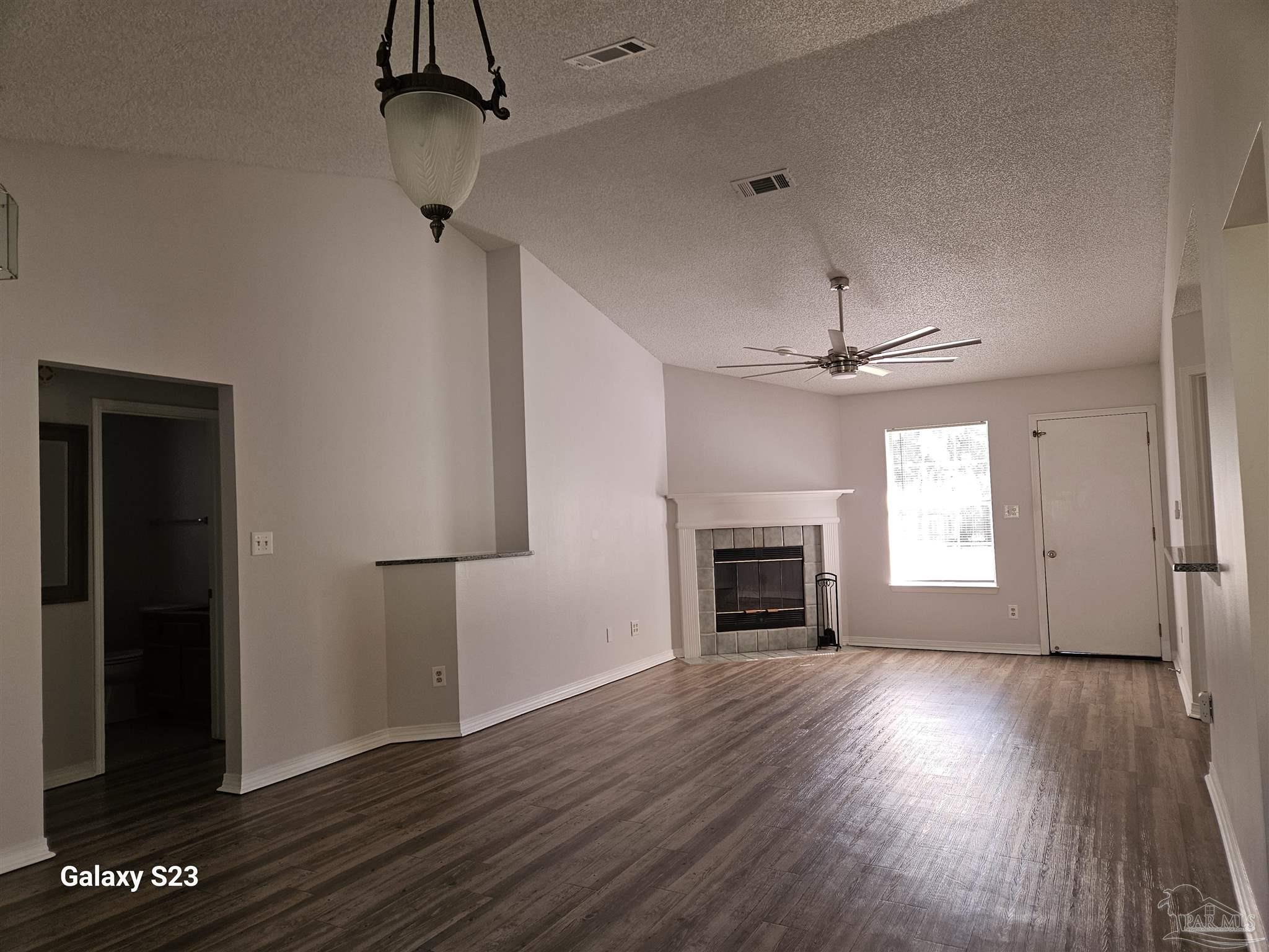 an empty room with wooden floor fireplace and windows