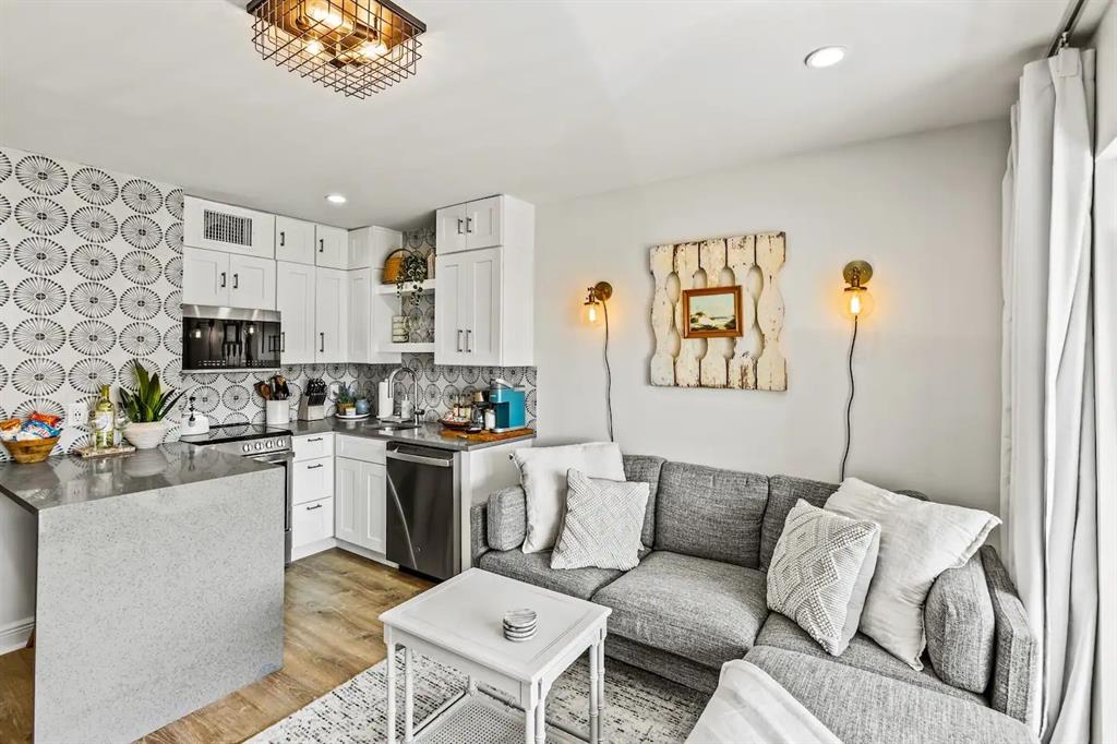 a living room with stainless steel appliances furniture a rug and a kitchen view