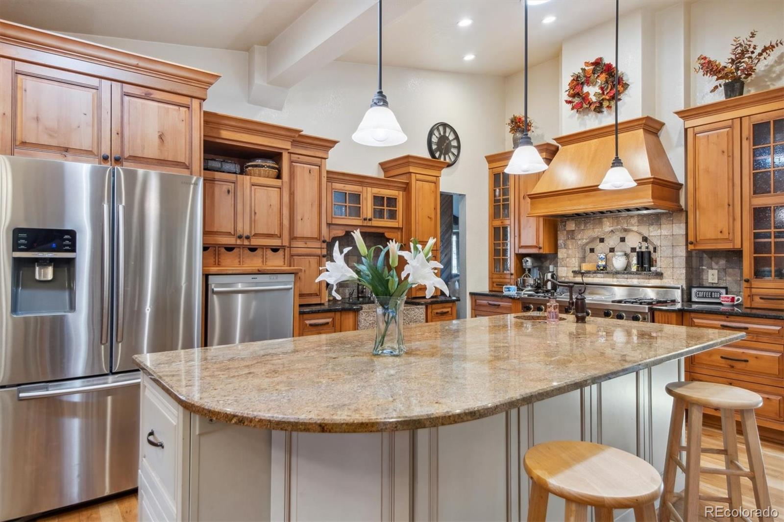 a kitchen with stainless steel appliances granite countertop a kitchen island a stove a refrigerator a dining table and chairs with wooden floor