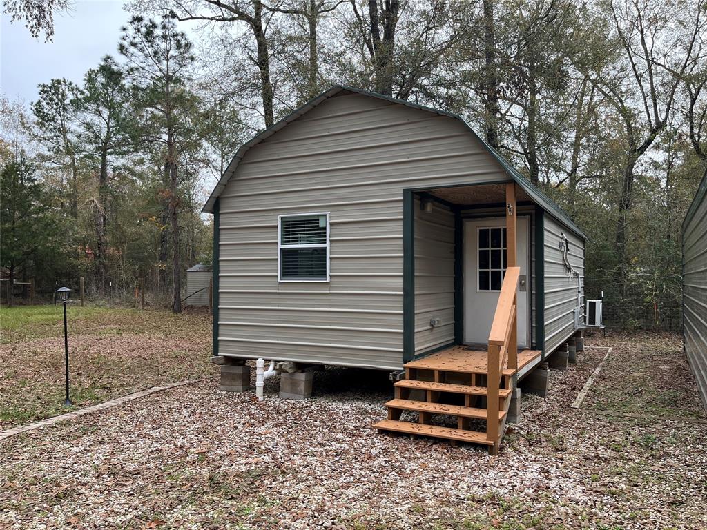 This efficiency tiny home with a metal exterior, surrounded by trees! . Featuring a front porch with wooden steps and a simple, natural landscape. Ideal for a cozy retreat or minimalist living.