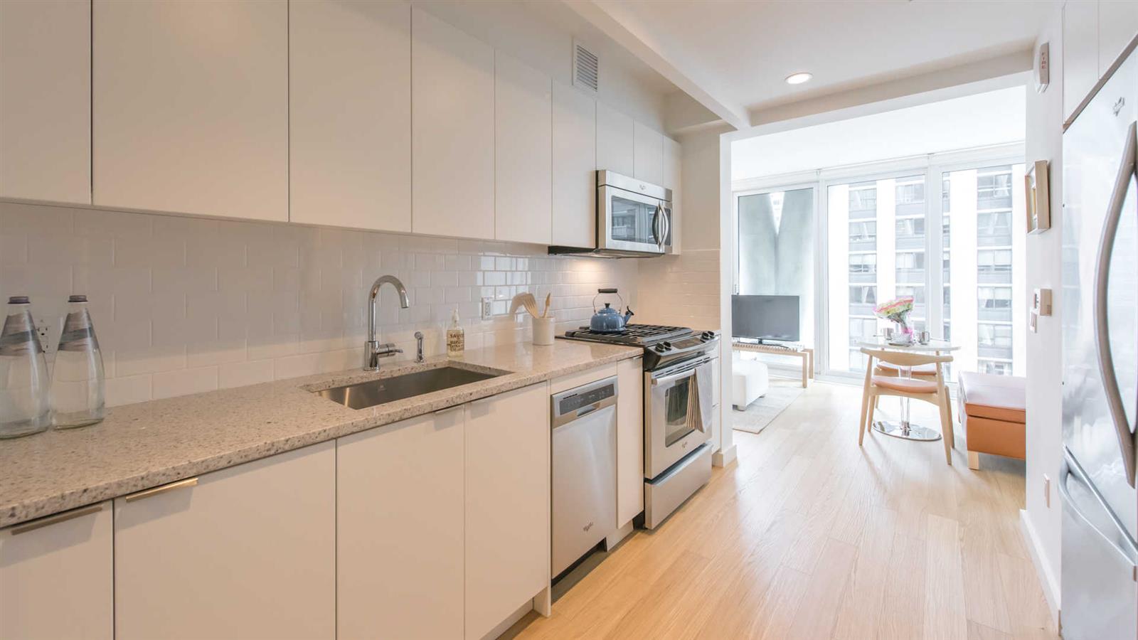 a kitchen with a sink dishwasher a stove and white cabinets with wooden floor