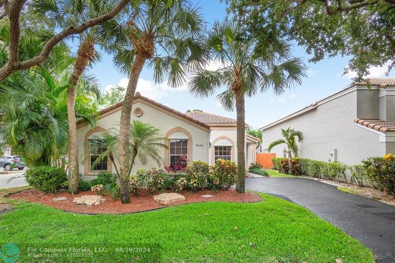 a front view of yellow house with a yard and palm trees