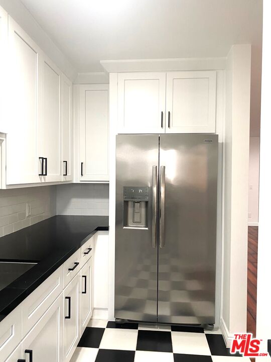 a kitchen with granite countertop a refrigerator and white cabinets