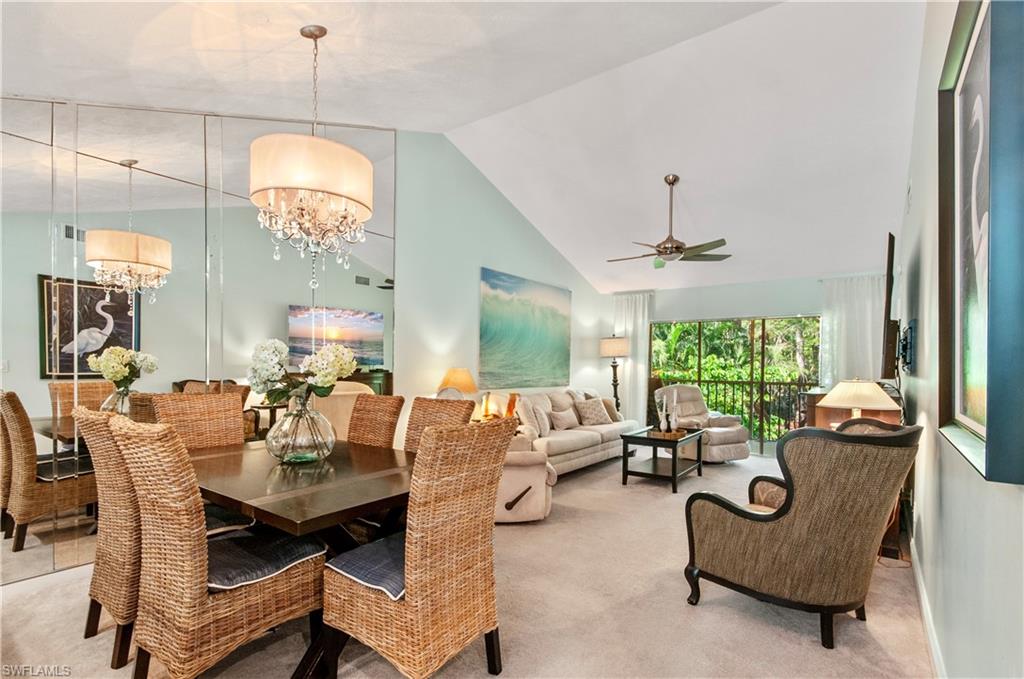 Carpeted dining area featuring ceiling fan with notable chandelier and high vaulted ceiling