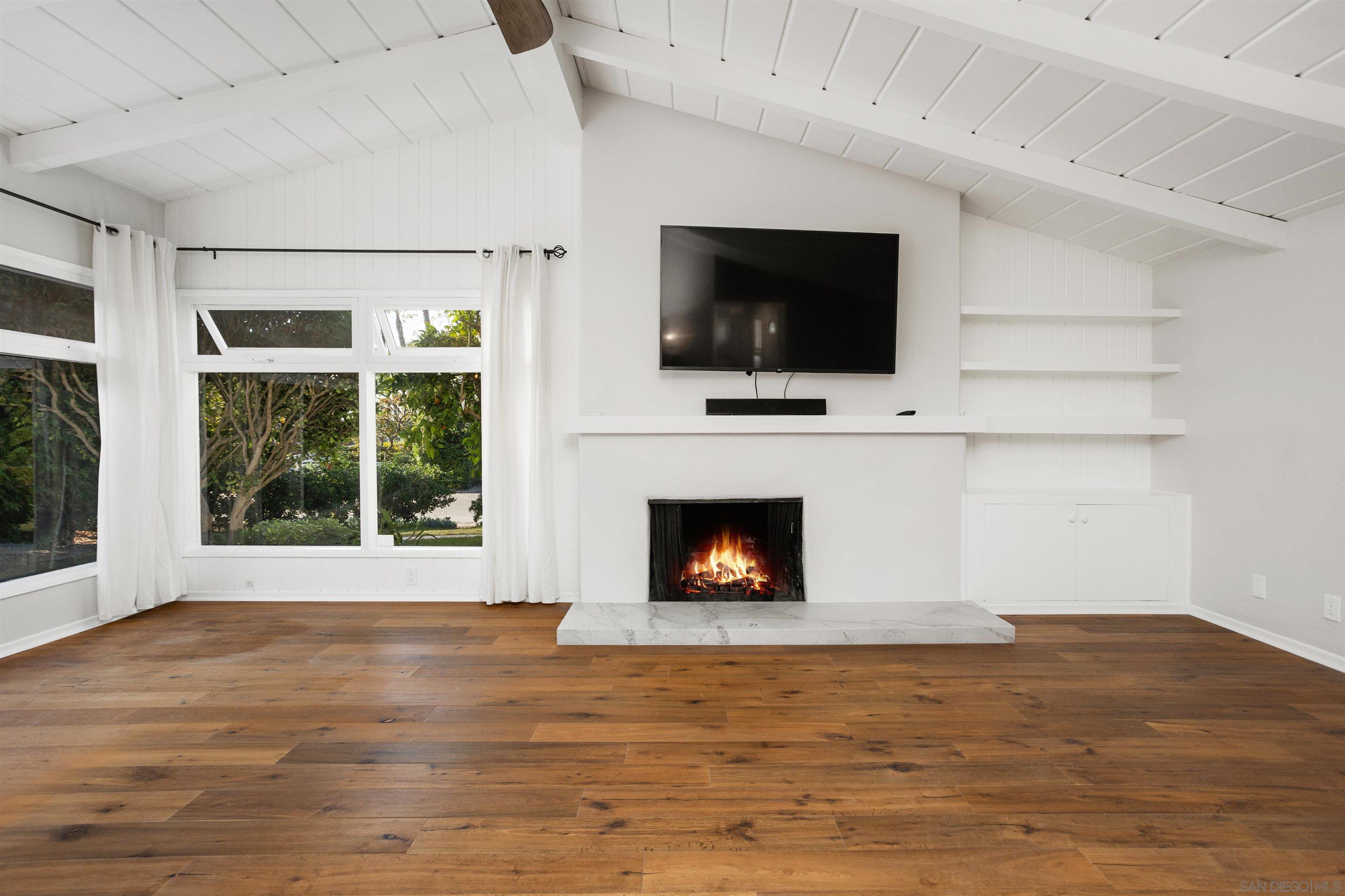 a view of an empty room with wooden floor fireplace and a window