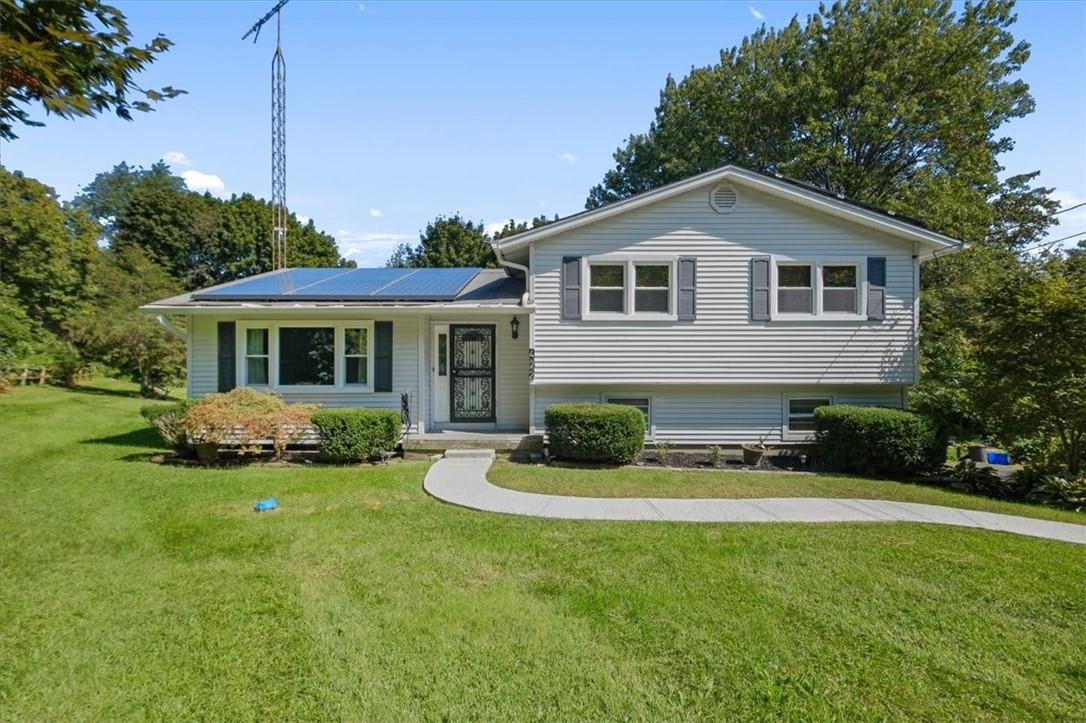 Tri-level home featuring a front lawn and solar panels