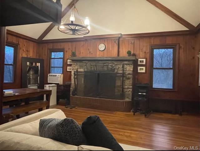 Living room featuring beamed ceiling, cooling unit, a stone fireplace, and hardwood / wood-style floors