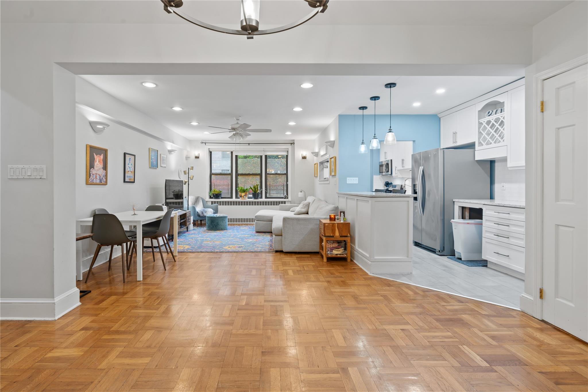 Living room with light parquet flooring and ceiling fan with notable chandelier