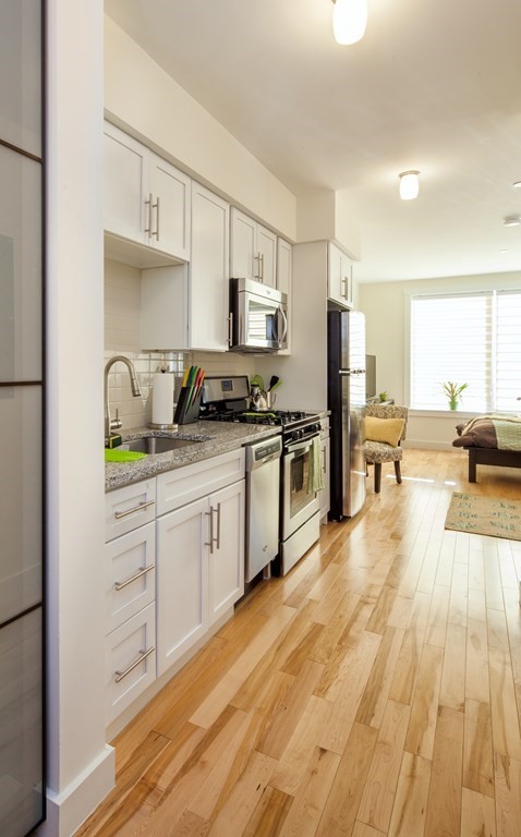 a kitchen with stainless steel appliances granite countertop a stove a sink and white cabinets with wooden floor