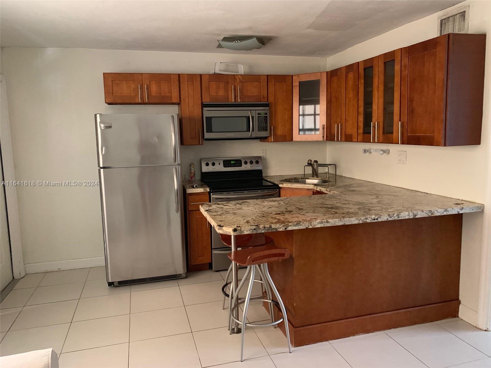 a kitchen with kitchen island granite countertop a refrigerator a stove and a sink with wooden cabinets