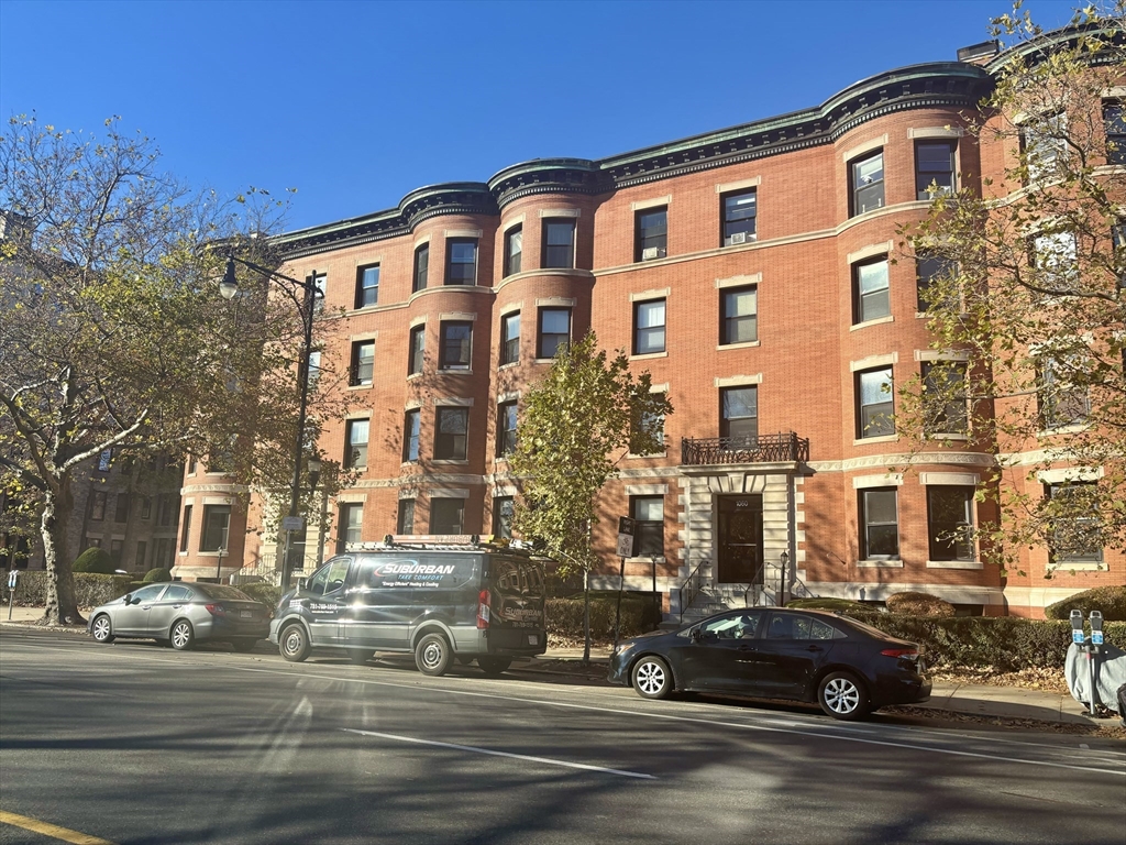 a front view of a building with lot of cars and trees