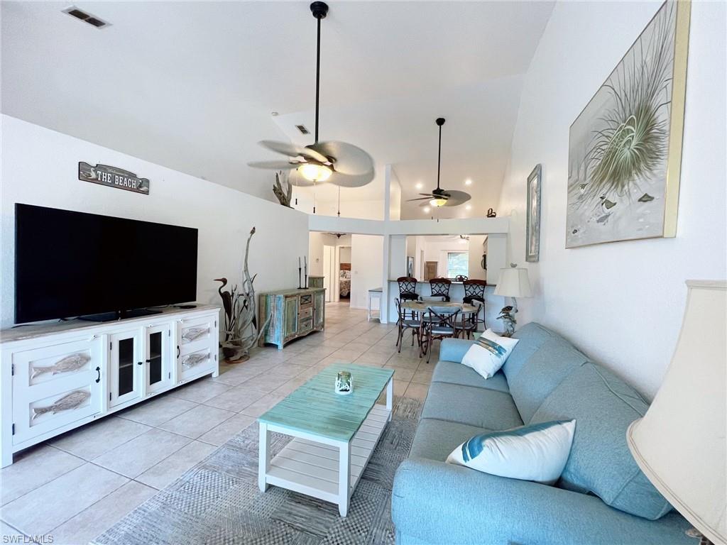 Living room featuring light tile patterned flooring, ceiling fan, and high vaulted ceiling