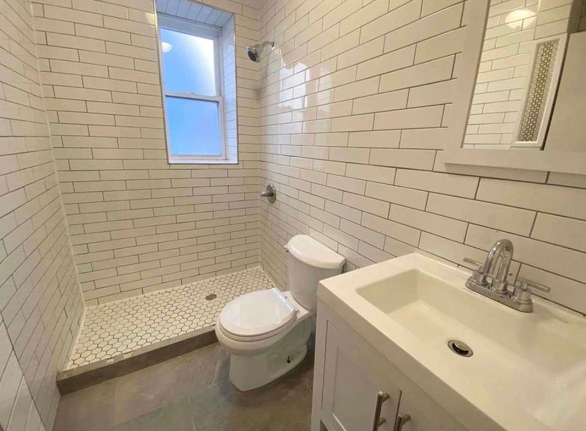 Bathroom featuring tiled shower, vanity, toilet, and tile walls