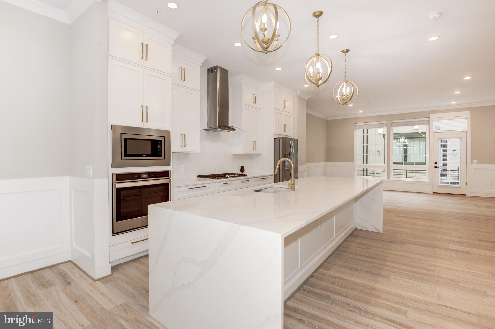 a large white kitchen with a large kitchen island white cabinetry and stainless steel appliances