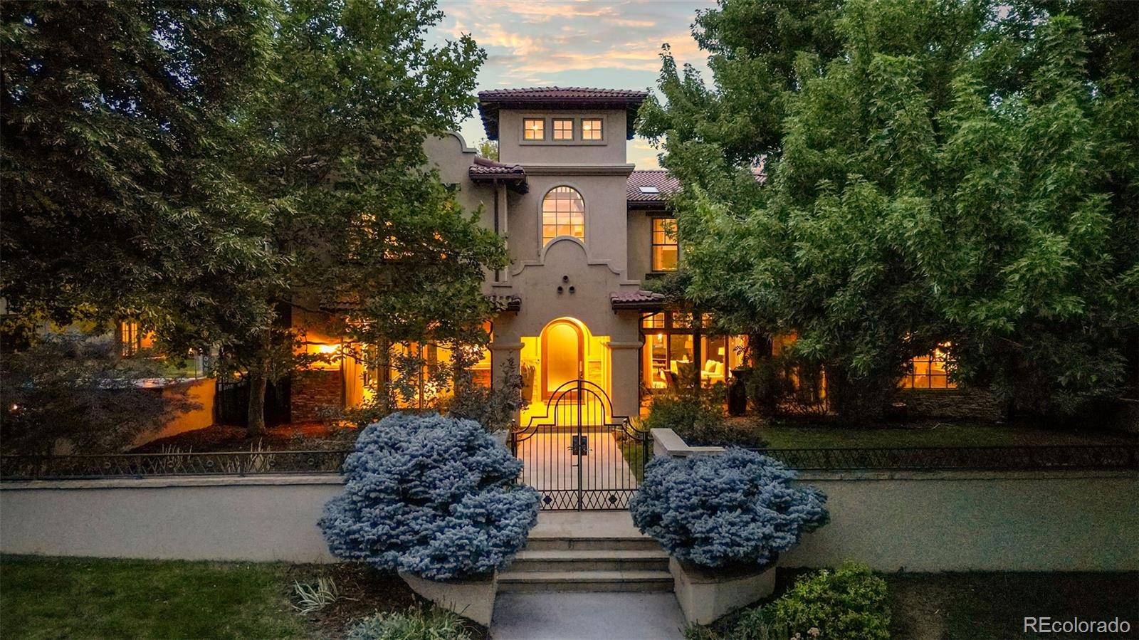 a front view of a house with large trees and plants