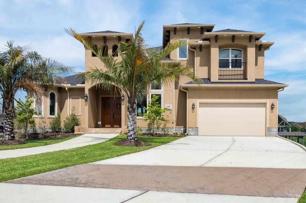 This is a modern two-story home featuring a stucco exterior with stone accents, a three-car garage, and lush landscaping with mature palm trees. The home has a welcoming entrance with a large wooden front door.