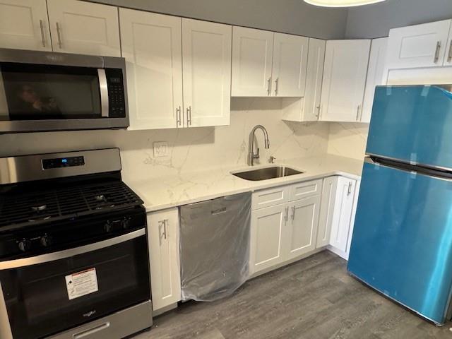 Kitchen featuring white cabinetry, sink, hardwood / wood-style floors, decorative backsplash, and appliances with stainless steel finishes